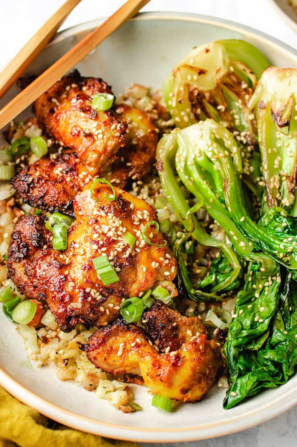 Air fried chicken nestled with rice and bok choy, with chopsticks across edge of plate.