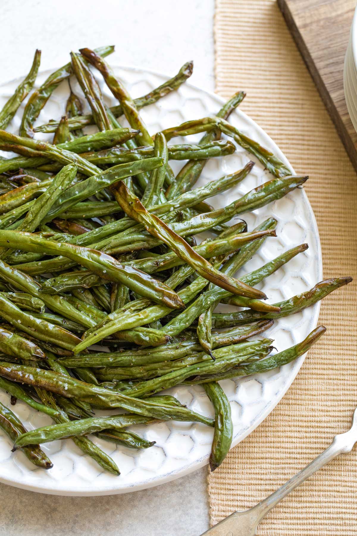 Overhead of plate filled with air fryer green beans, laying partially on yellow placemat.