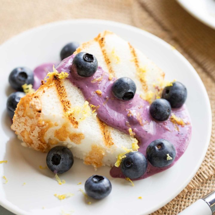 Grilled slice of angel food cake on a small white plate with all the toppings, ready to eat