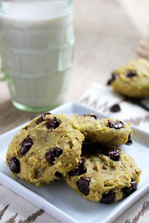 Closeup of three cookies on small, square white plate with glass of milk and additional cookie in background.