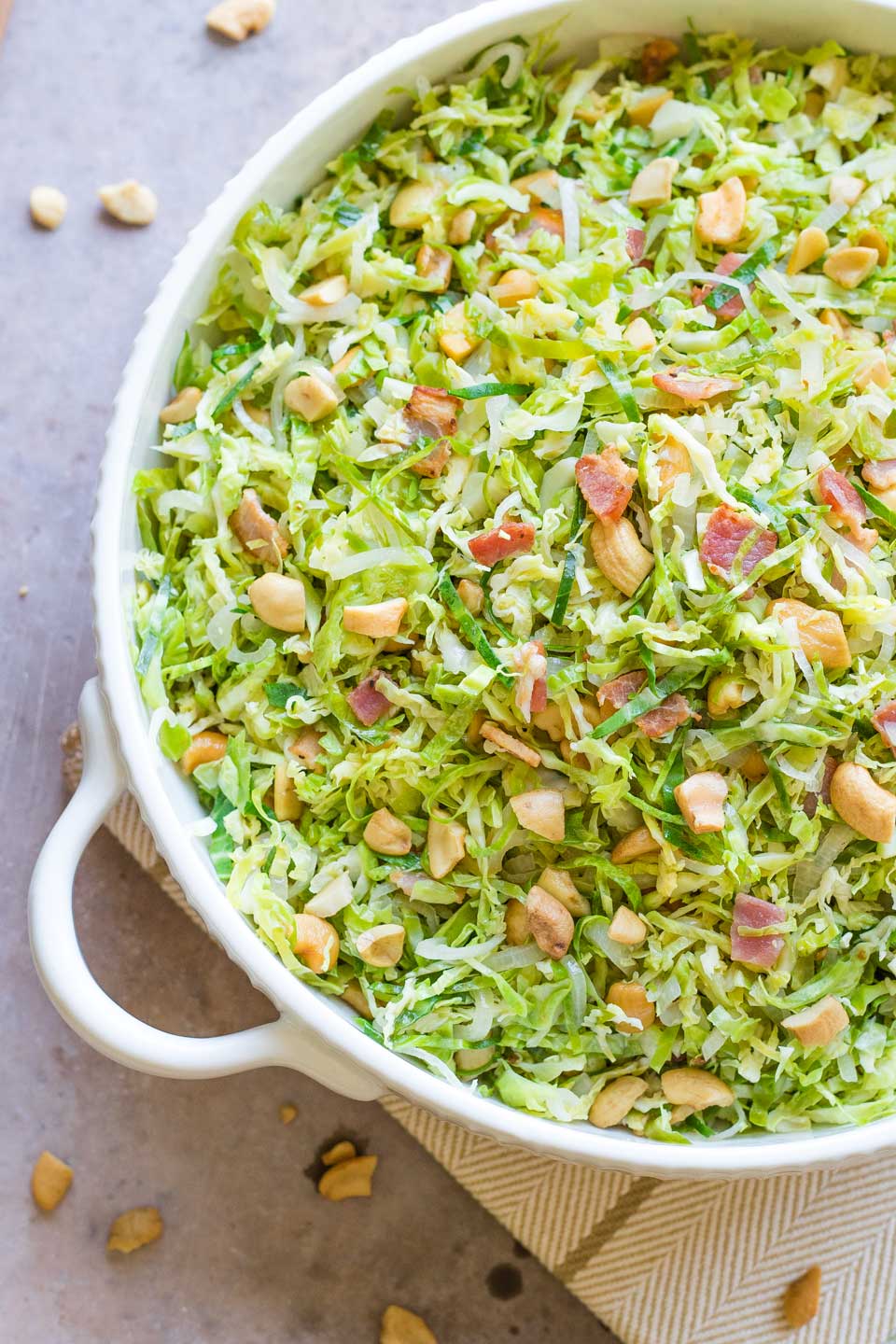 Bacon Brussel sprouts recipe piled in handled white serving bowl on a herringbone striped cloth.