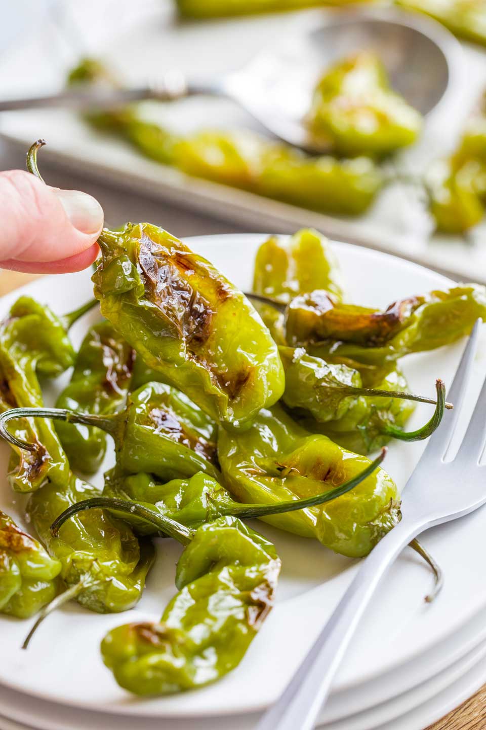 Fingers plucking one shishito pepper off an appetizer plate full.