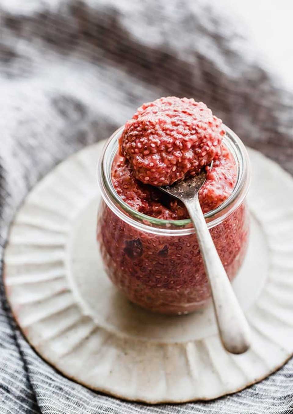 One pudding jar on a scalloped white plate, with a spoonful of pudding laid across the top so you can see the texture of chia.