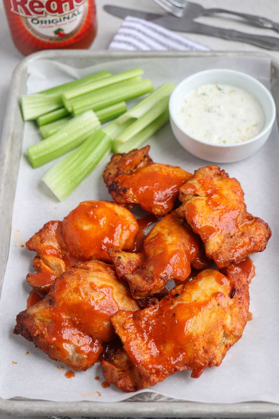 Several buffalo chicken pieces on paper-lined tray with ranch and celery sticks.