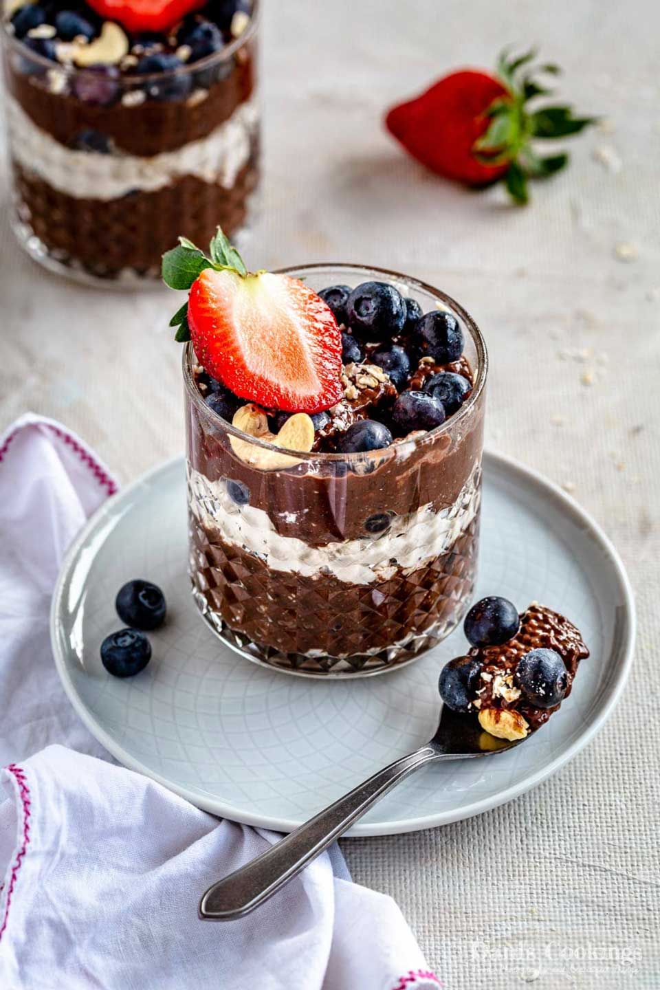 Textured glass full of pudding on a white plate, with a spoonful of chia pudding and extra berries alongside.