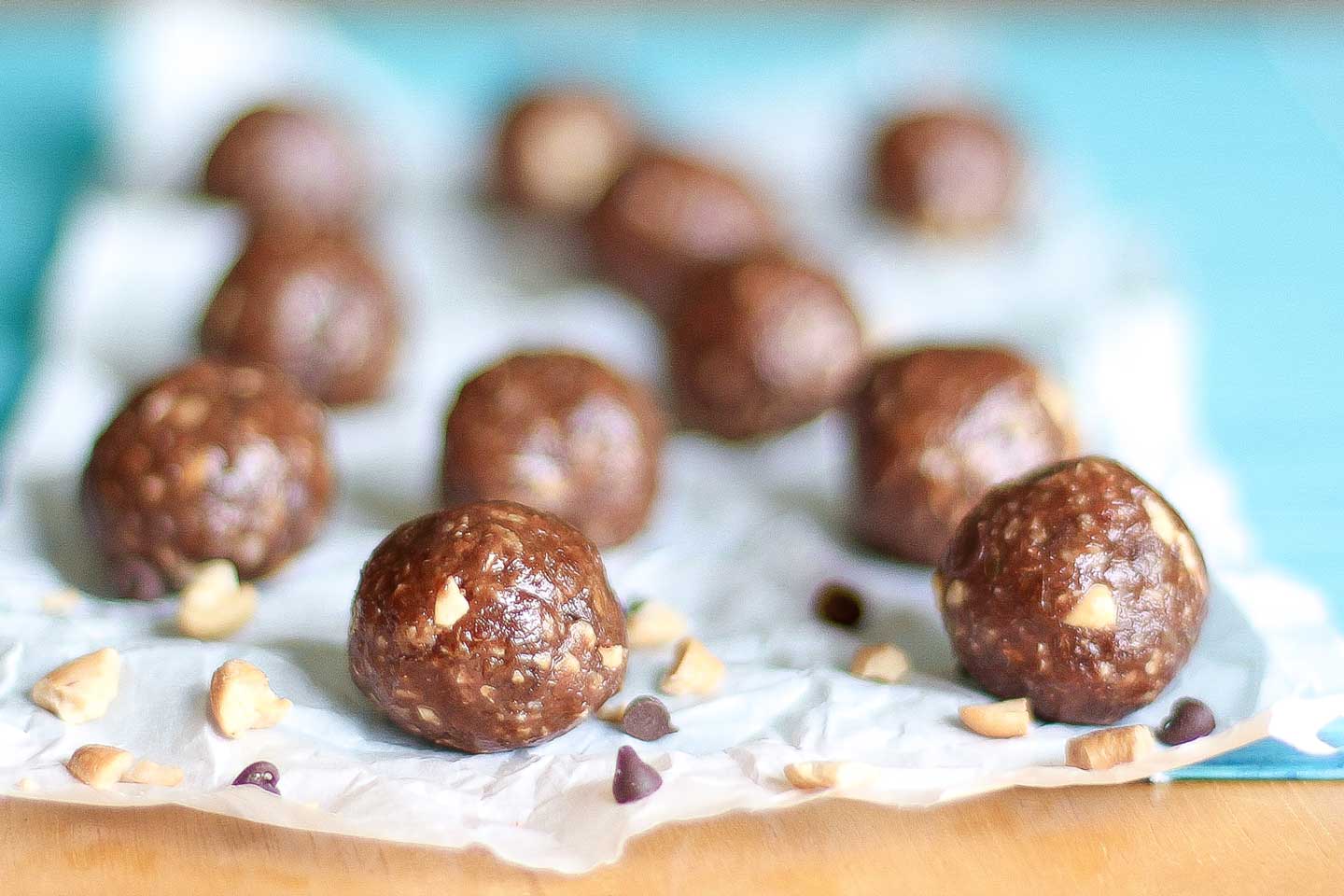 11 finished energy balls laying on crumpled white parchment on top of a turquoise cloth.