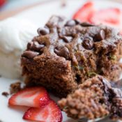 closeup of one bite on a fork, laying on a white plate next to the rest of the piece of cake, along with sliced berries and a bit of ice cream