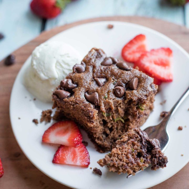 one piece of cake on a white plate with a forkful laying alongside, garnished with a scoop of ice cream and sliced strawberries