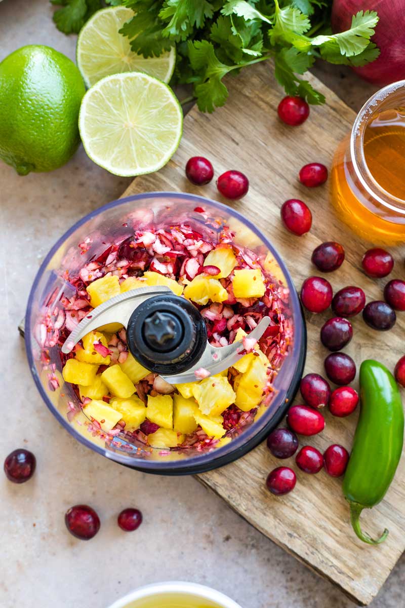 Overhead of processor with partially chopped cranberries and pineapple added on top.