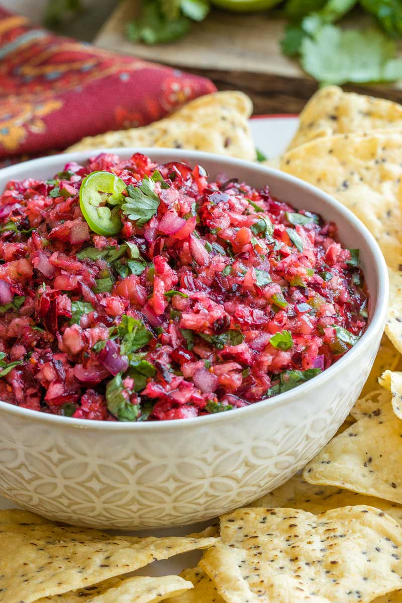 Closeup of salsa in bowl surrounded by chips, so you can really see the texture of cranberry bits with flecks of jalapeno and cilantro.