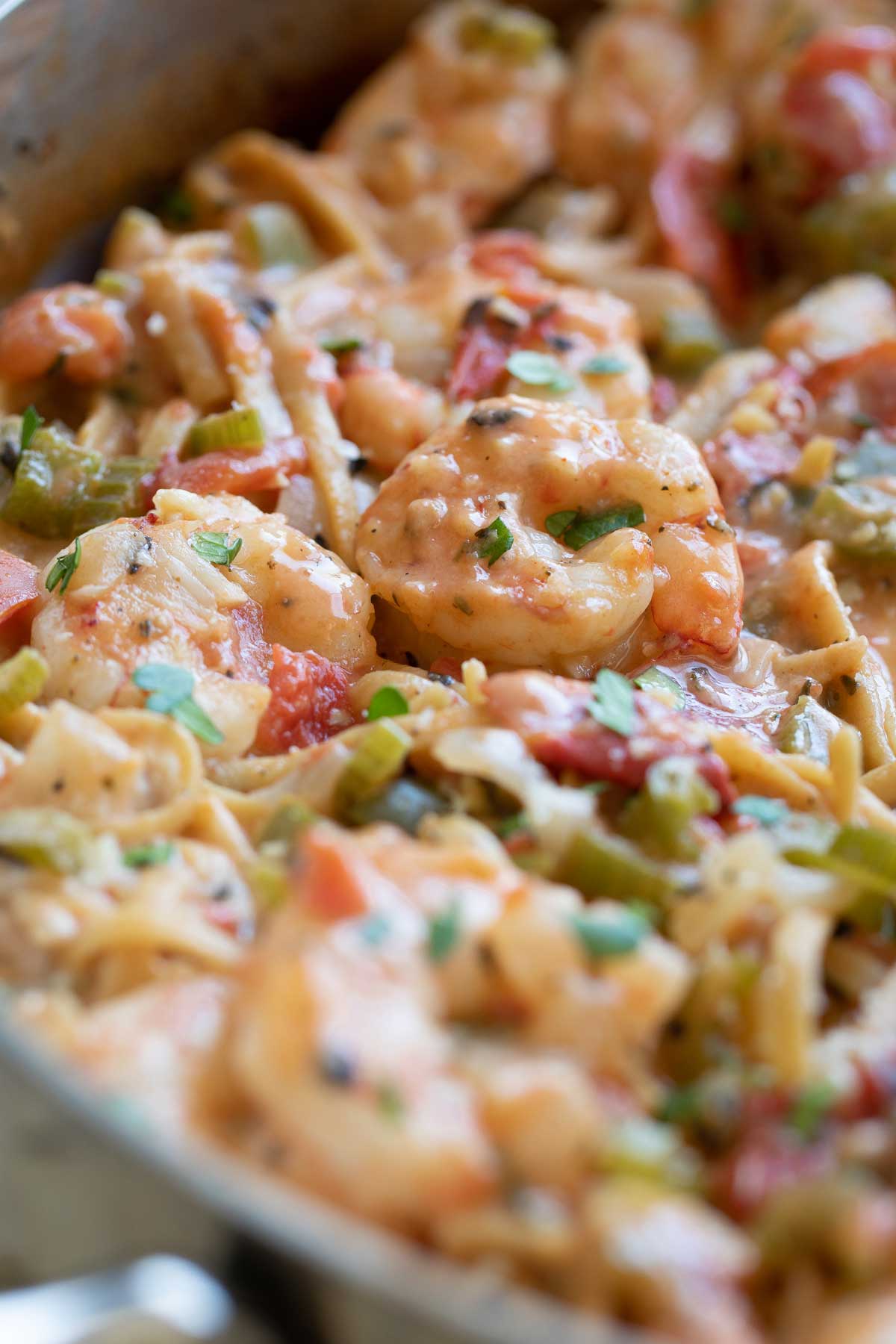 Closeup of the shrimp, still in the pan, sitting on top of the pasta and dotted with creamy sauce and bits of parsley.