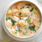 Overhead of a white bowl with creamy colored rim on cream napkin, with spoon above and fresh thyme sprigs at corner.