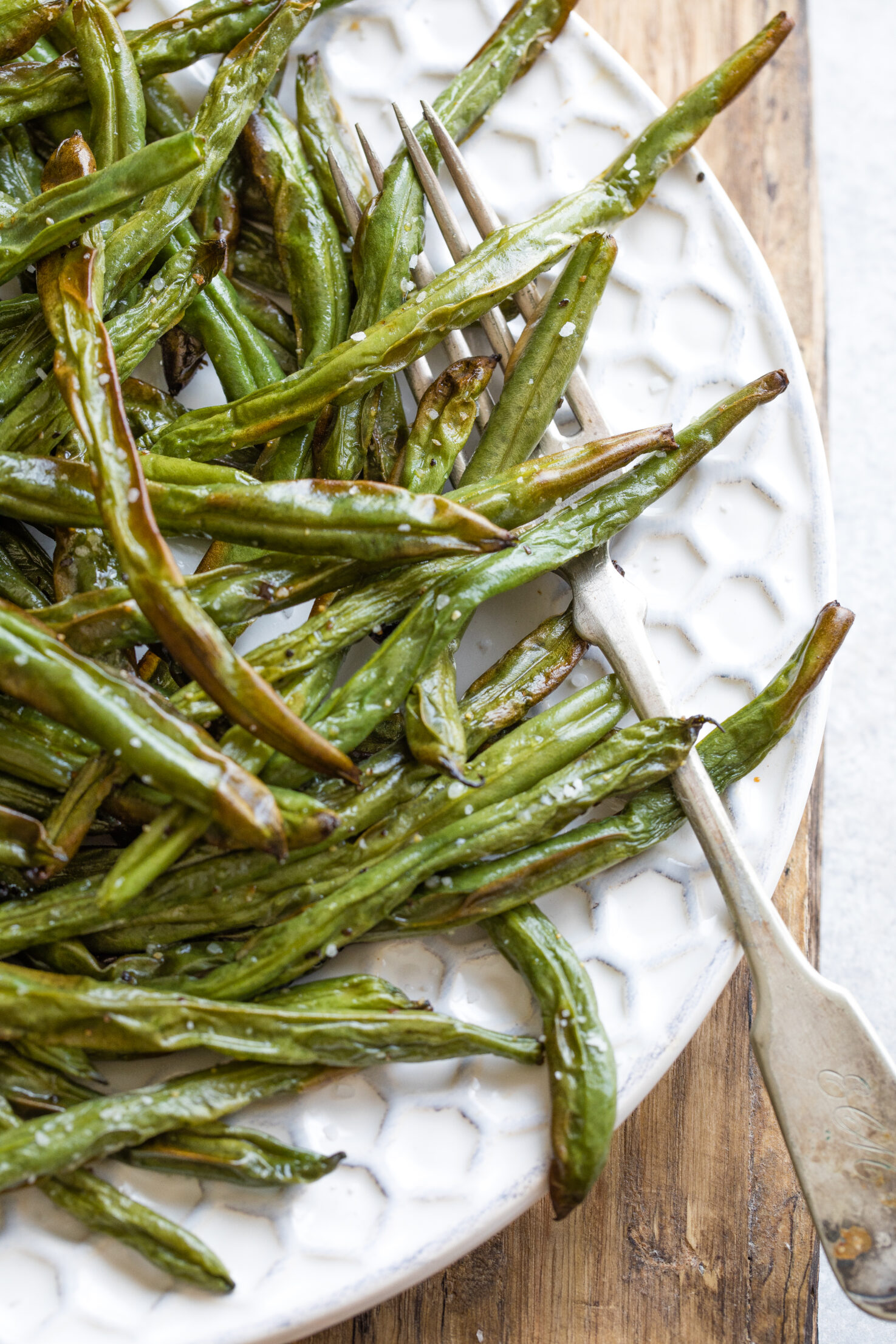 Closeup of right half of platter full of cooked beans, with antique serving fork entwined in them.