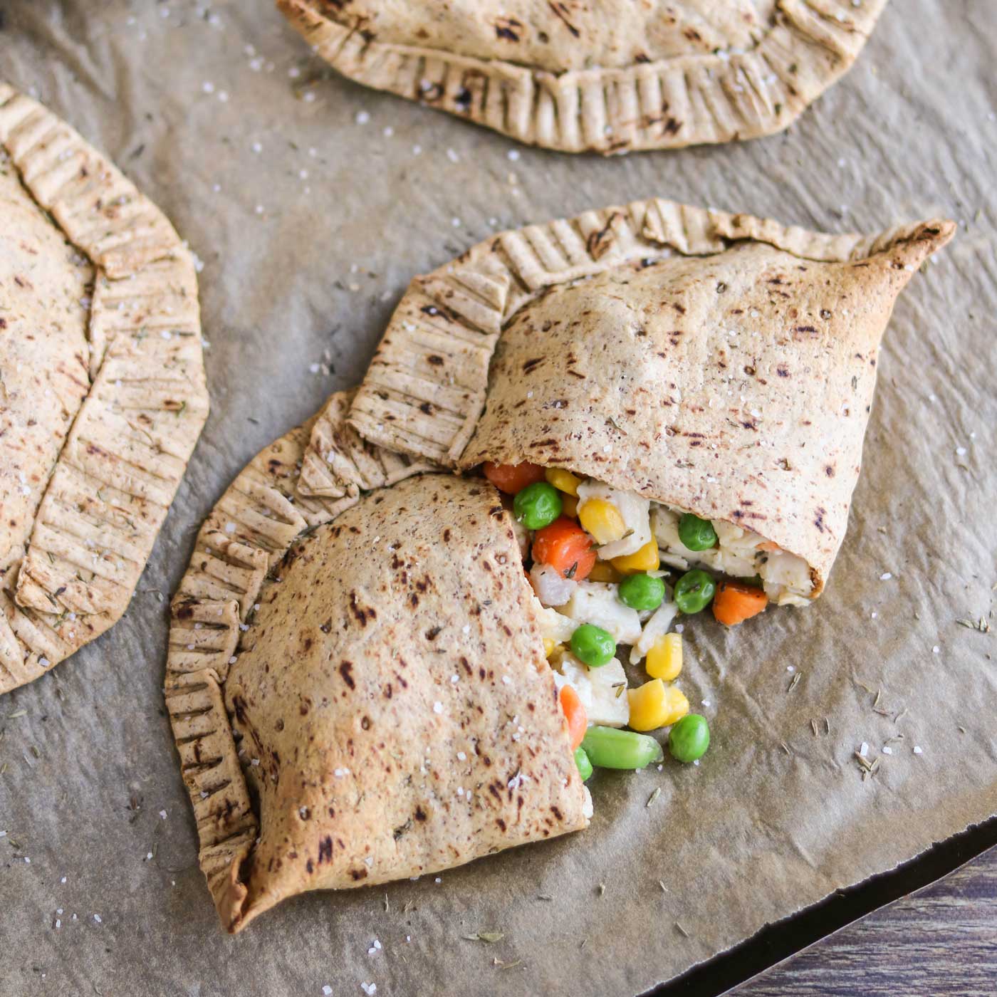 overhead of our Chicken Pot Pie Hand Pies recipe on a baking sheet, with on cut open to reveal the yummy chicken mixture inside