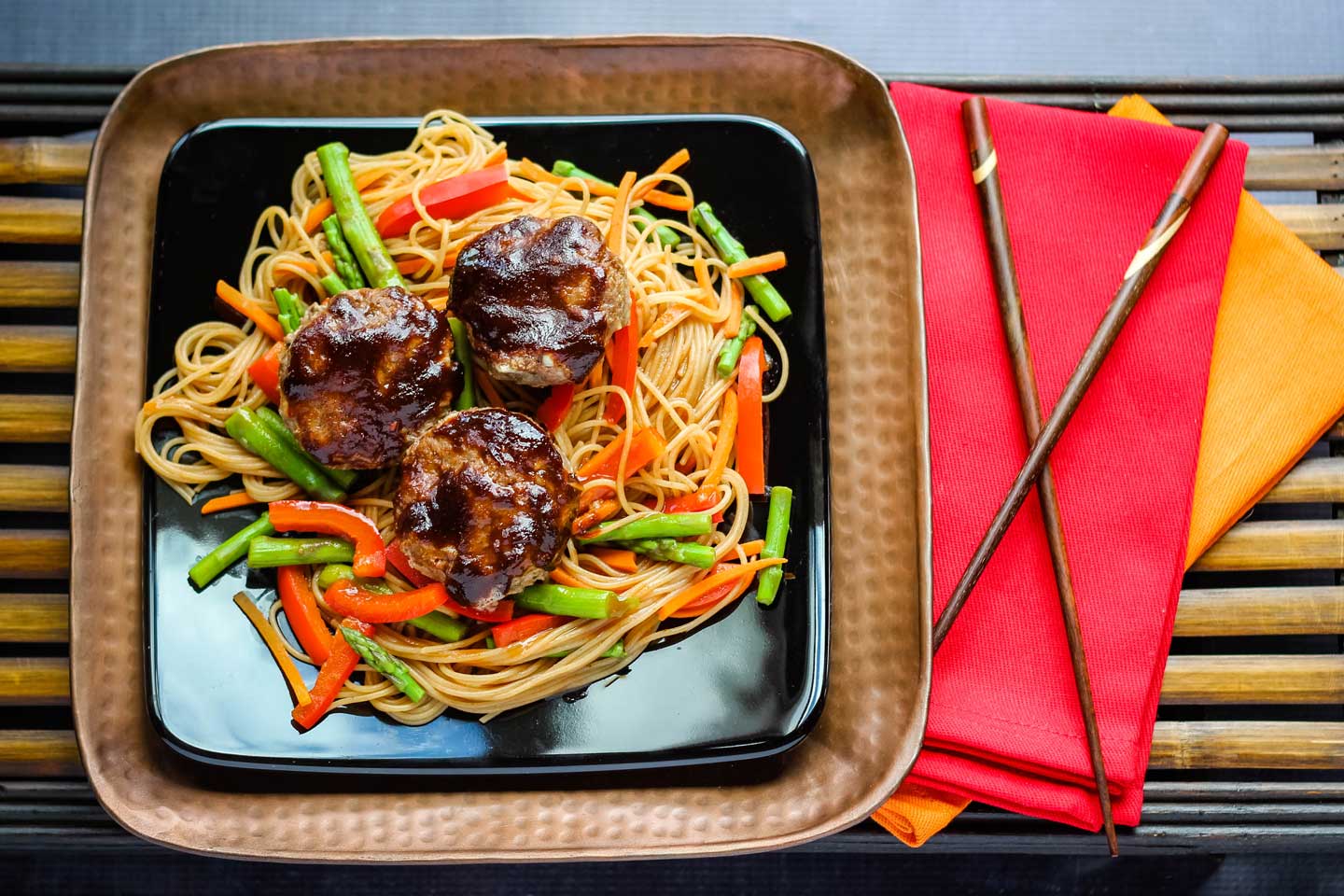 example of a healthy hamburger meat recipe - mini Asian Meatloaves plated on top of vegetables and noodles, next to napkins and chopsticks