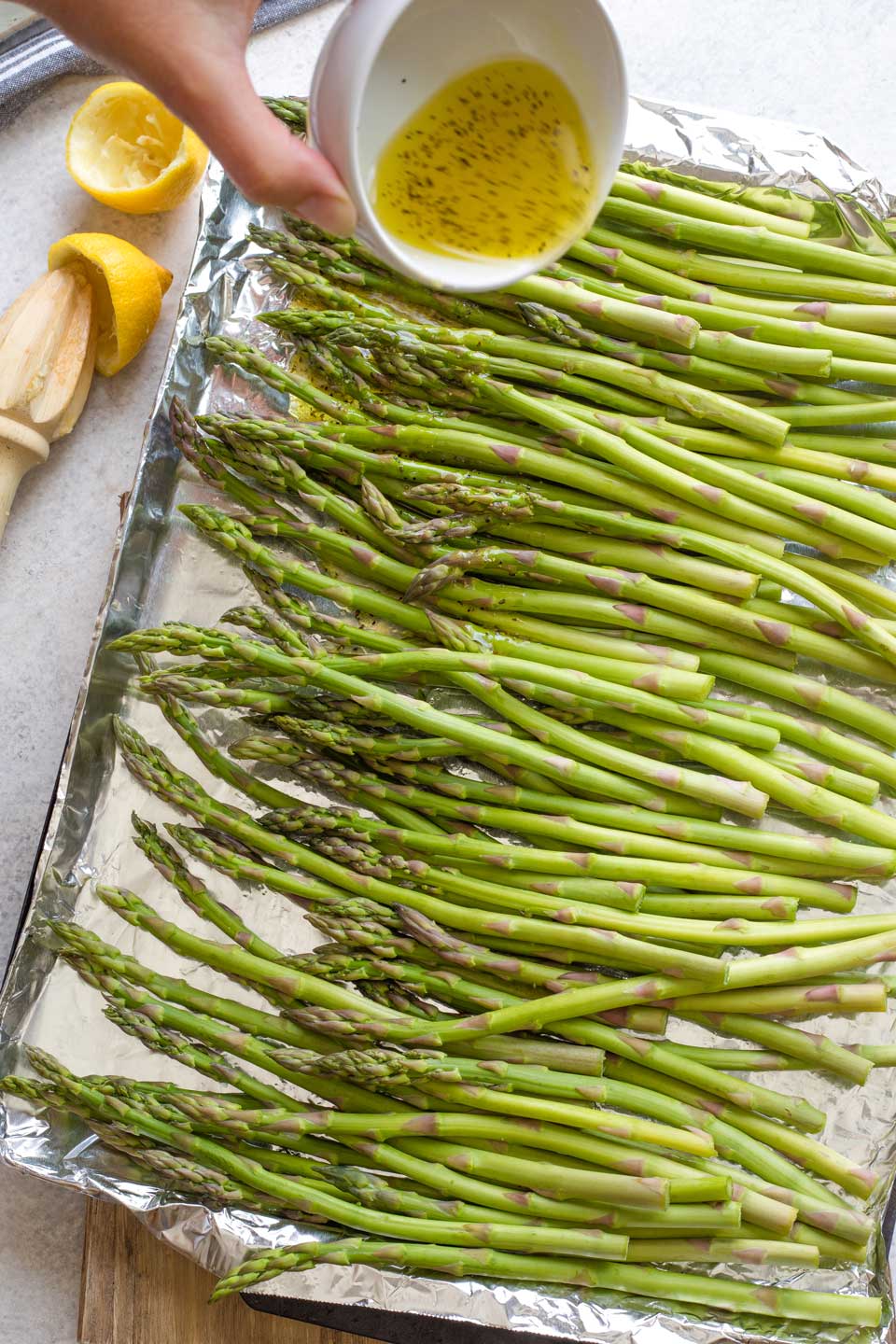 Hand pouring marinade on asparagus spread on foil-lined grill pan.