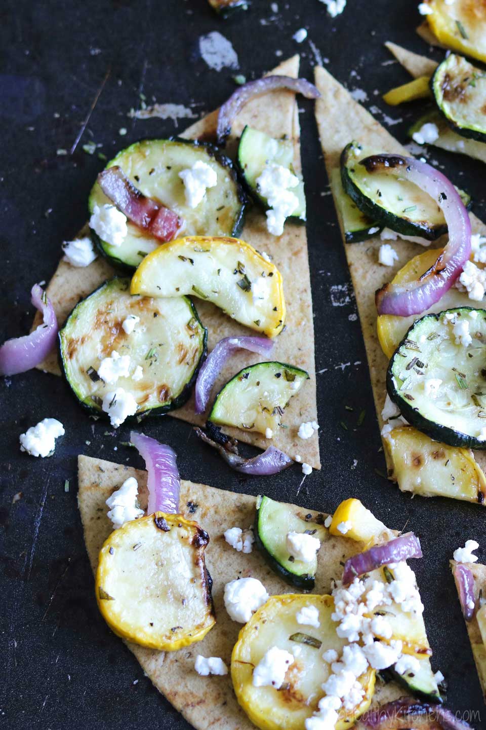 Closeup of one wedge of flatbread surrounded by others on black baking sheet.