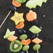 Four kebabs at various angles on black background, with fruit cutout of a bat from a green honeydew melon.