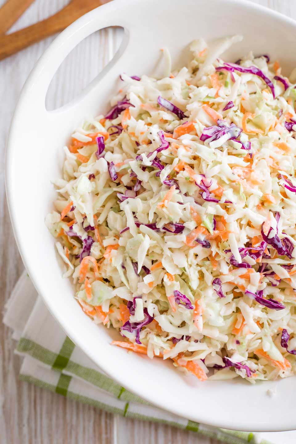 Overhead of a serving bowl of coleslaw sitting on a green-striped towel