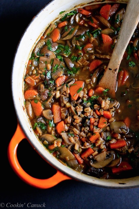 Overhead of left half of orange-enameled soup pot full of cooked soup with wooden spoon dipping in.