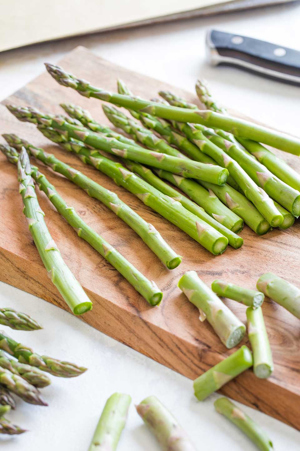 Asparagus spears on a cutting board, with the bottom inch or two of their stems just cut off.