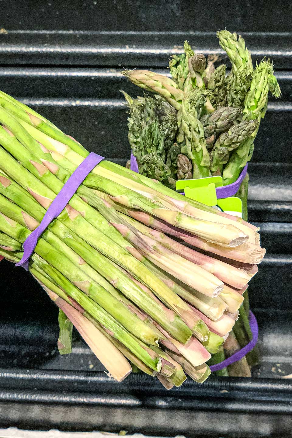 Closeup of the bottom of a bunch of asparagus at the store, showing how the bottoms are wrinkled and dried out.