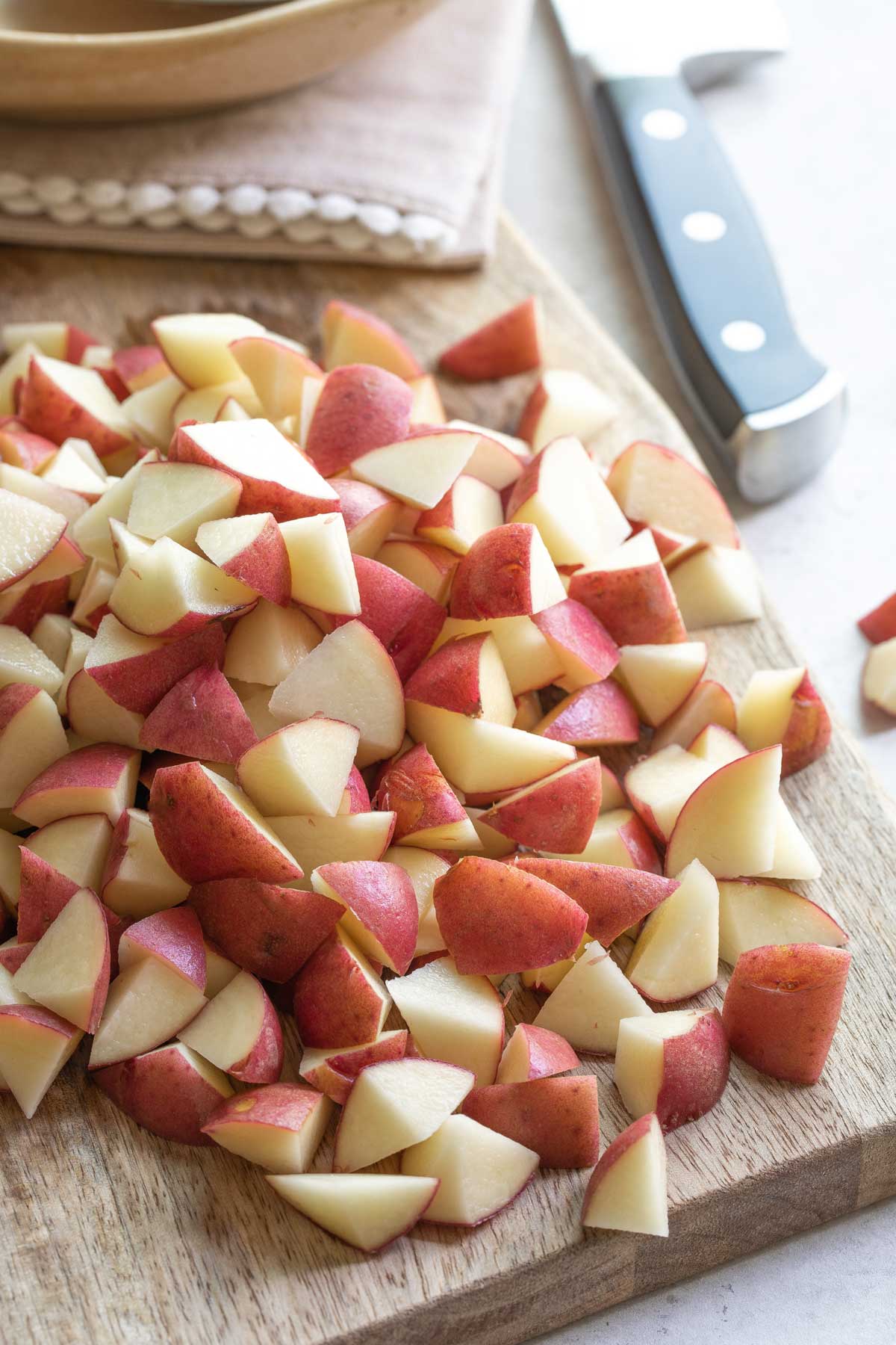 Chopped red potatoes on cutting board with knife in background.