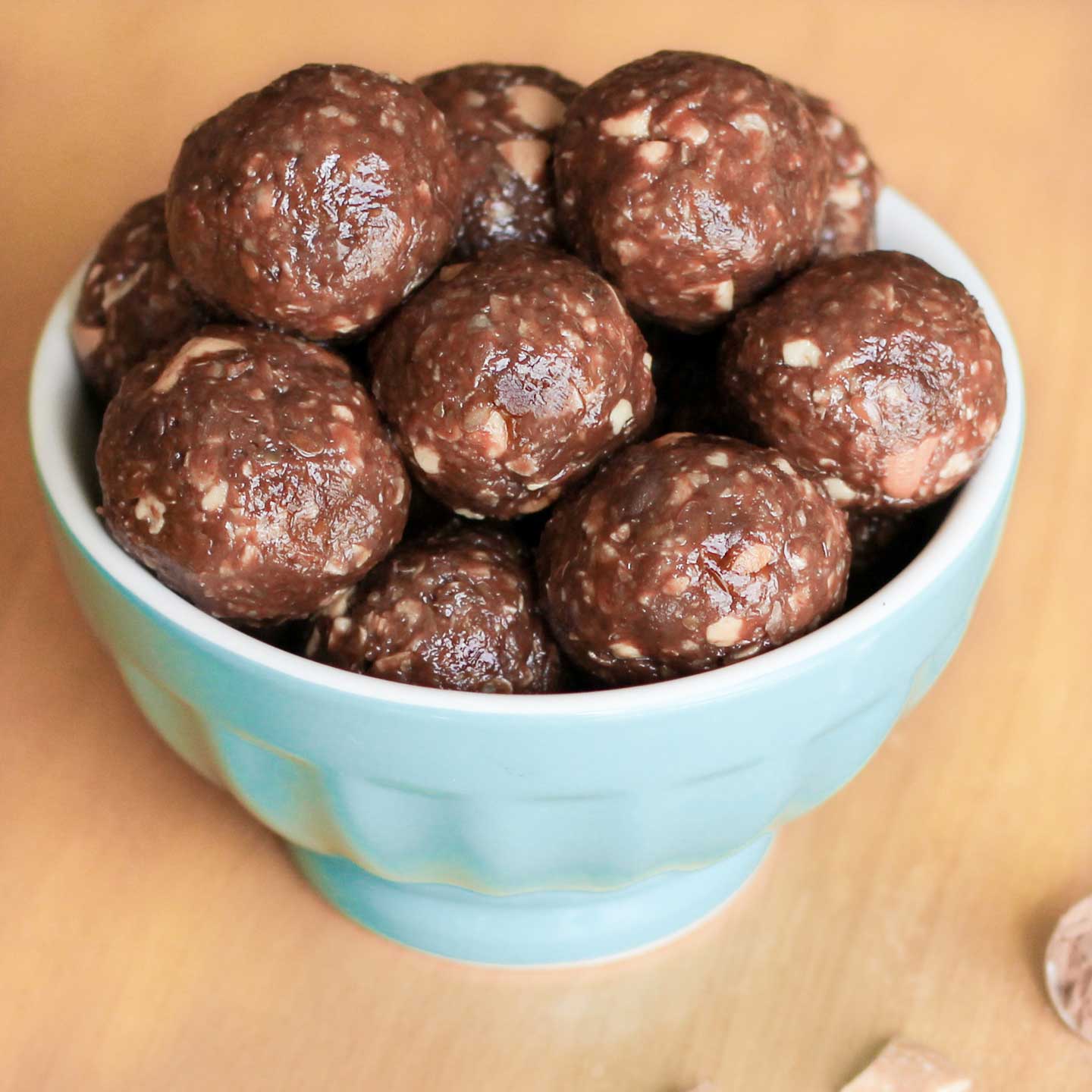 Blue bowl piled with finished energy balls on wood table.