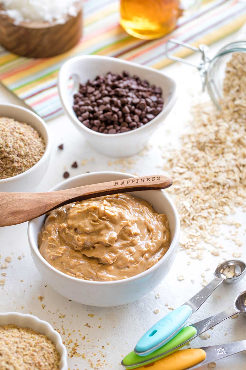 Ingredients for making energy balls, displayed in little bowls with colorful measuring spoons near.