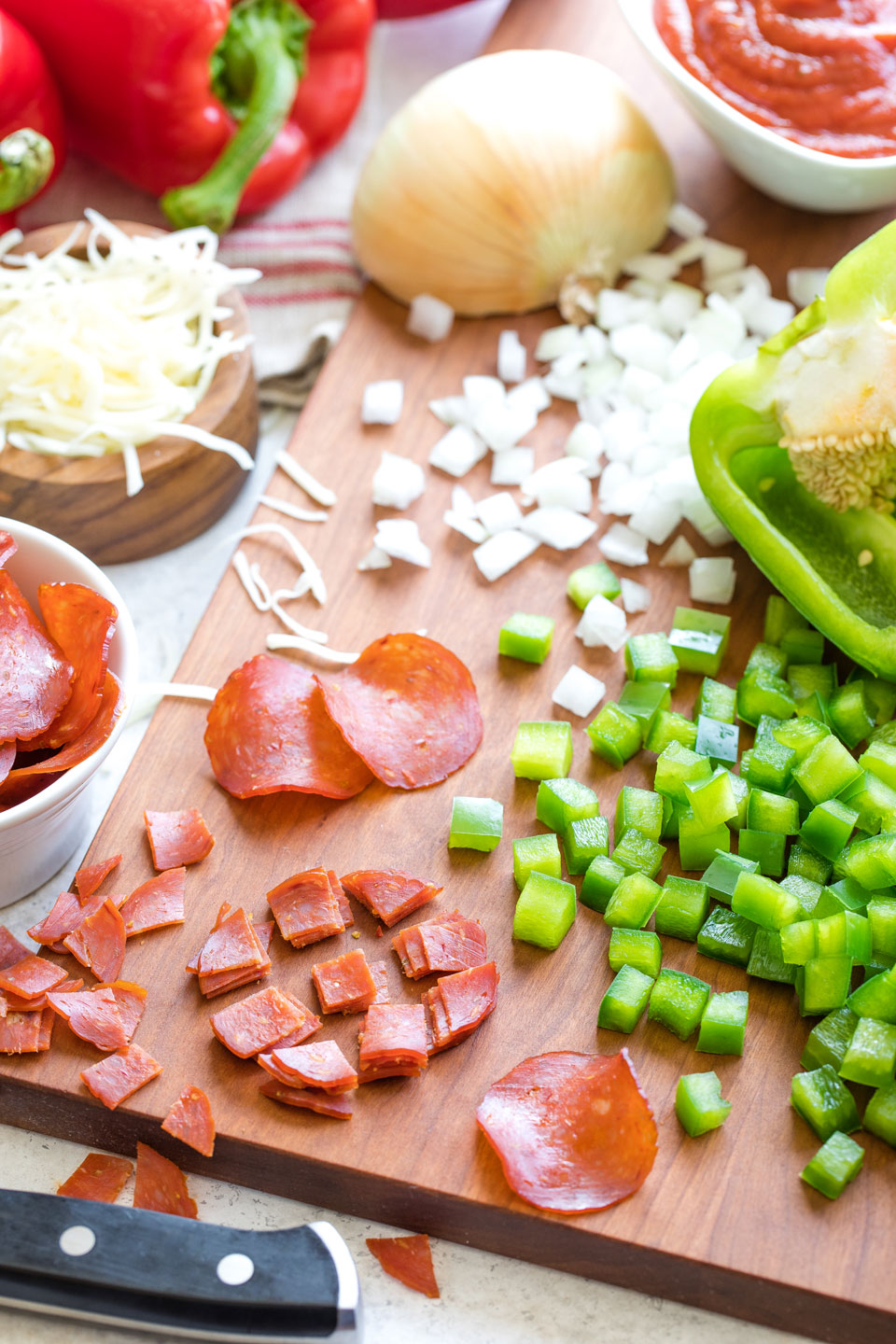 Cutting board surrounded by ingredients and covered in diced peppers, onions and pepperoni.