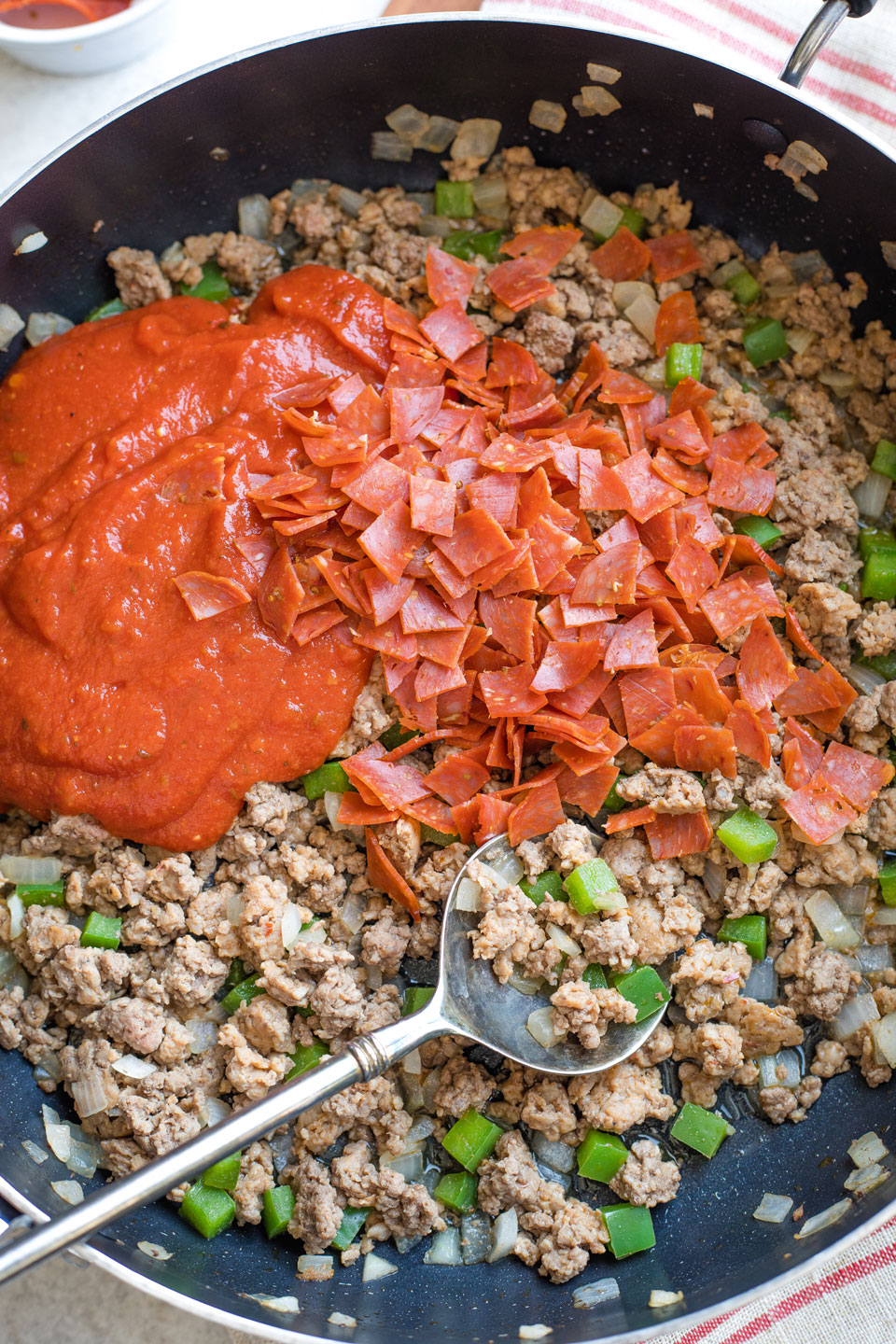 Adding Italian pizza sauce and pepperoni to pepper filling in skillet.