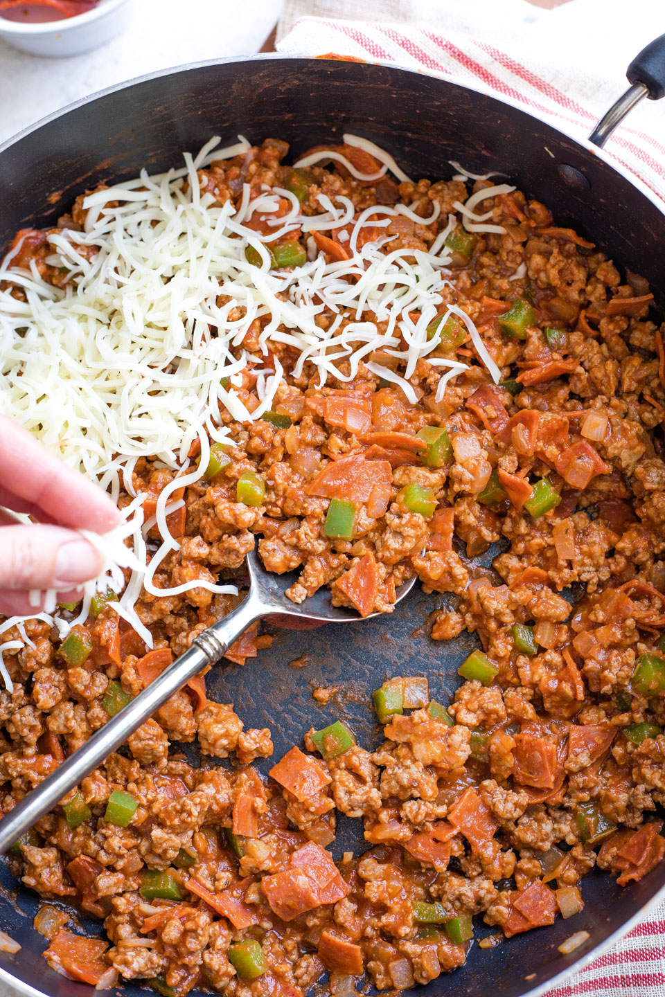 Hand sprinkling cheese on stuffing in skillet.