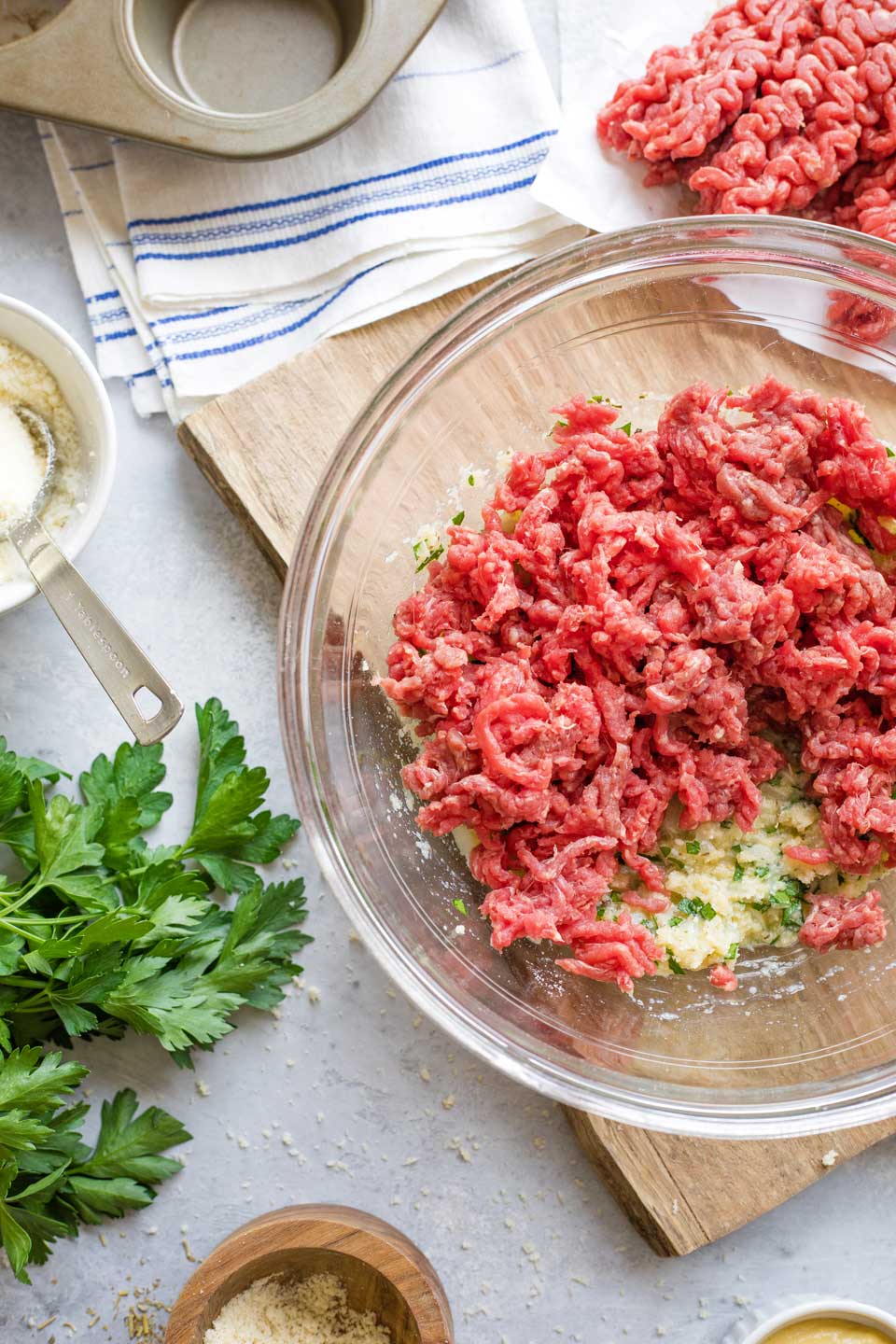 Ground beef crumbled into mixing bowl on top of other meatloaf ingredients.