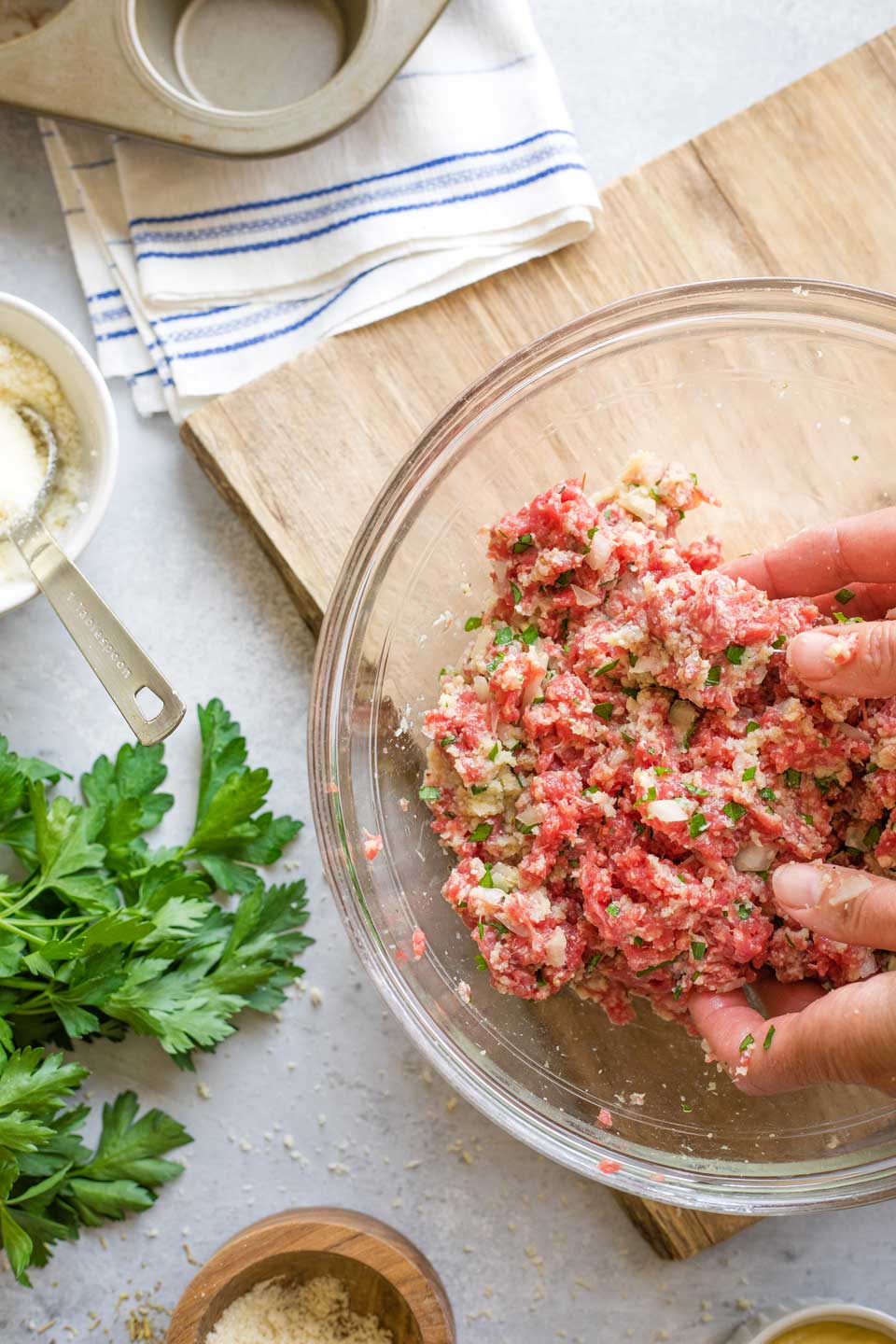 Two hands reaching into mixing bowl to combine meatloaf ingredients.