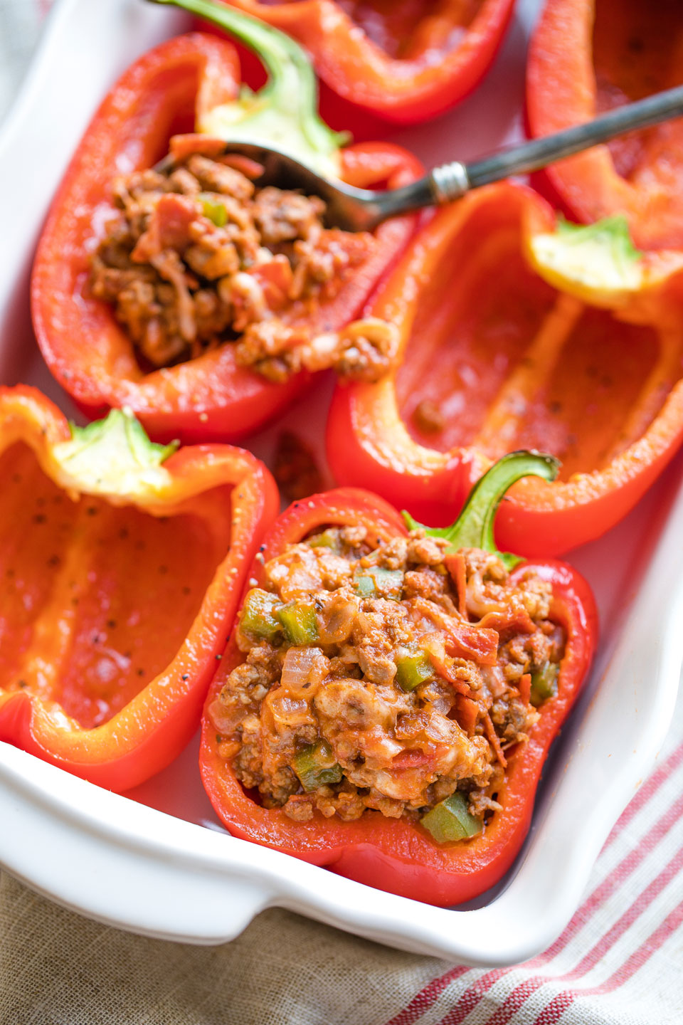 Six pepper halves in baking dish with two stuffed and the rest still empty.