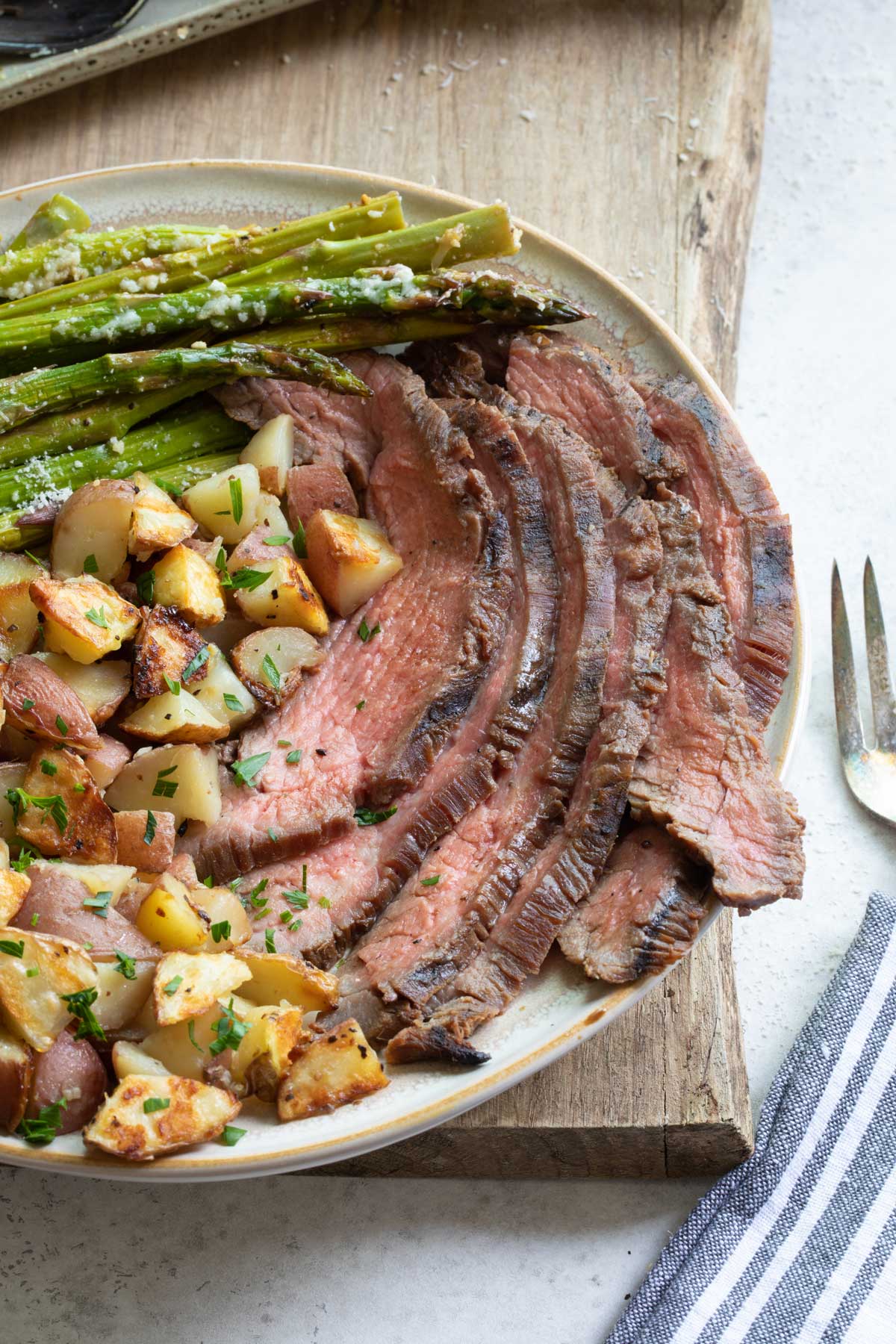 Six slices of beef on dinner plate with grilled potatoes and asparagus for complete meal.