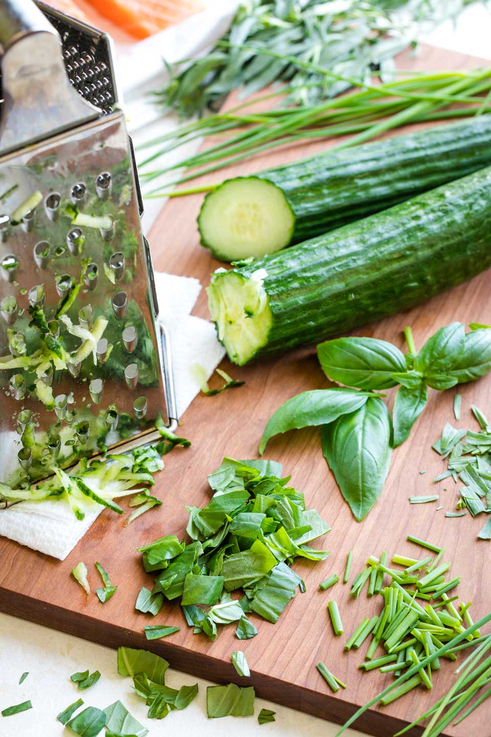 Herbs and cucumbers for the tzatziki sauce laying on a cutting board, mostly chopped and grated and ready to be put in the food processor.