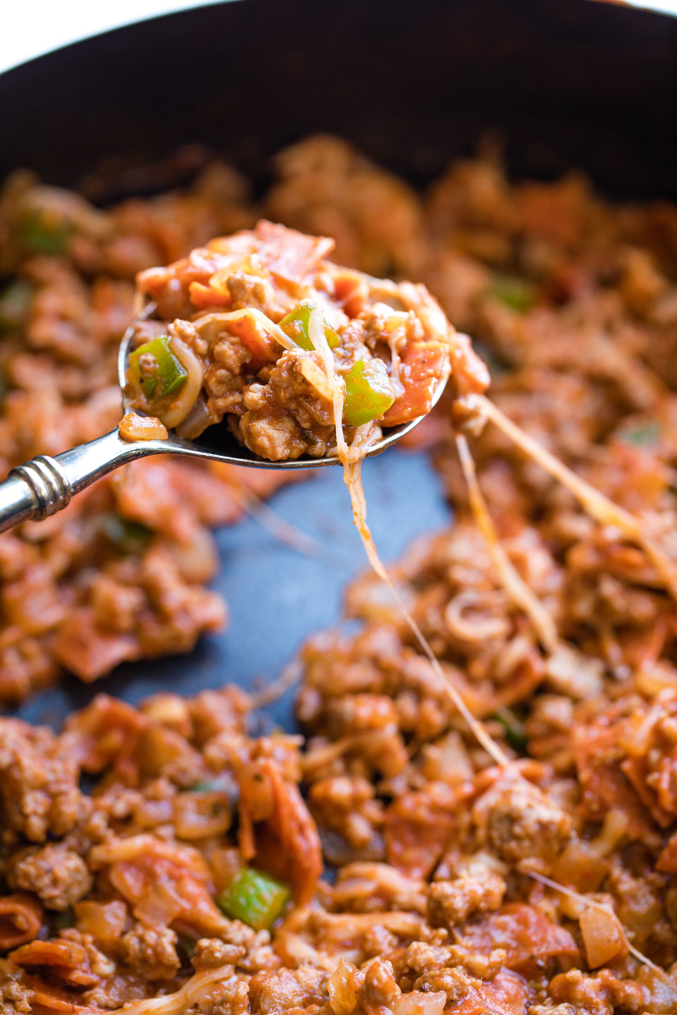 Spoon lifting some stuffing from skillet with cheese pull.