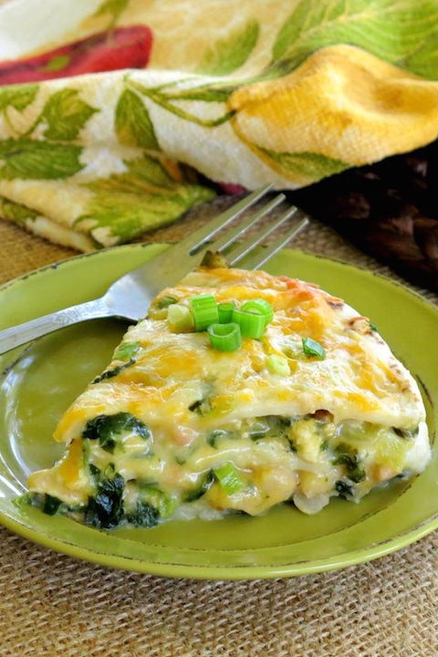 One slice of enchilada pie on pea-green plate with fork, colorful napkin in background.