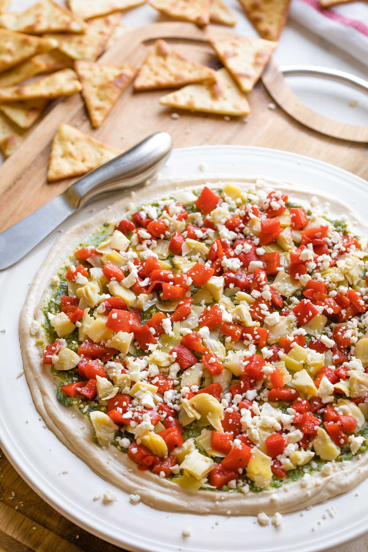 Finished recipe on white rimmed platter on cutting board with triangular pita chips and appetizer spreader.