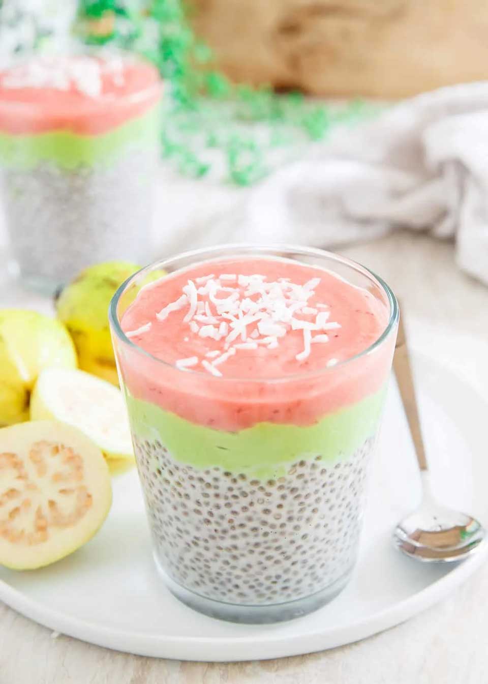 Pudding in a tapered glass with cut guavas and a spoon on a white tray.