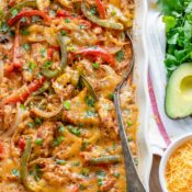 Flatlay of finished casserole with serving spoon tucked in on wooden board; Mexican toppings waiting alongside.