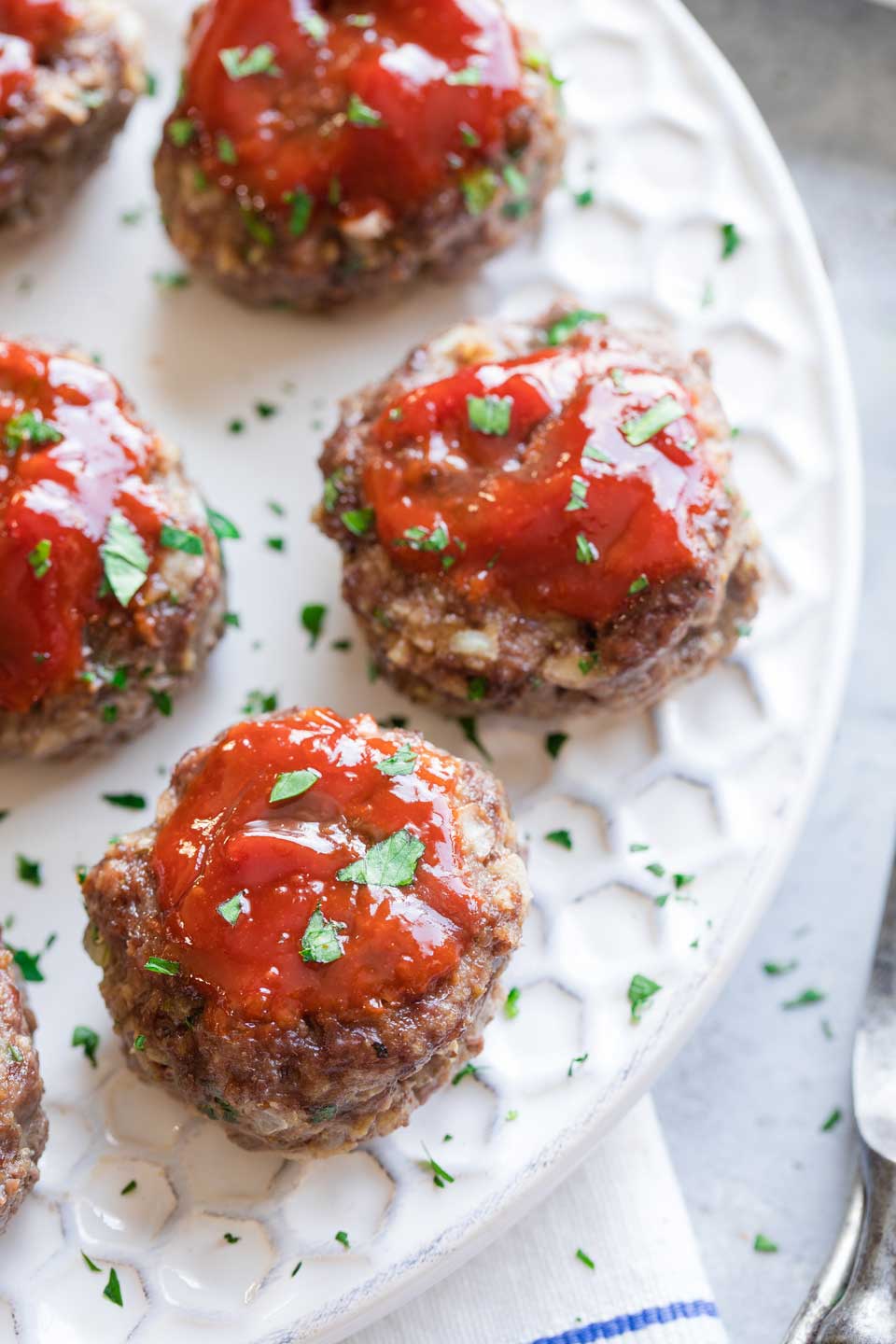 Closeup of a few meatloaf patties on white serving tray, sprinkled with chopped fresh parsley.