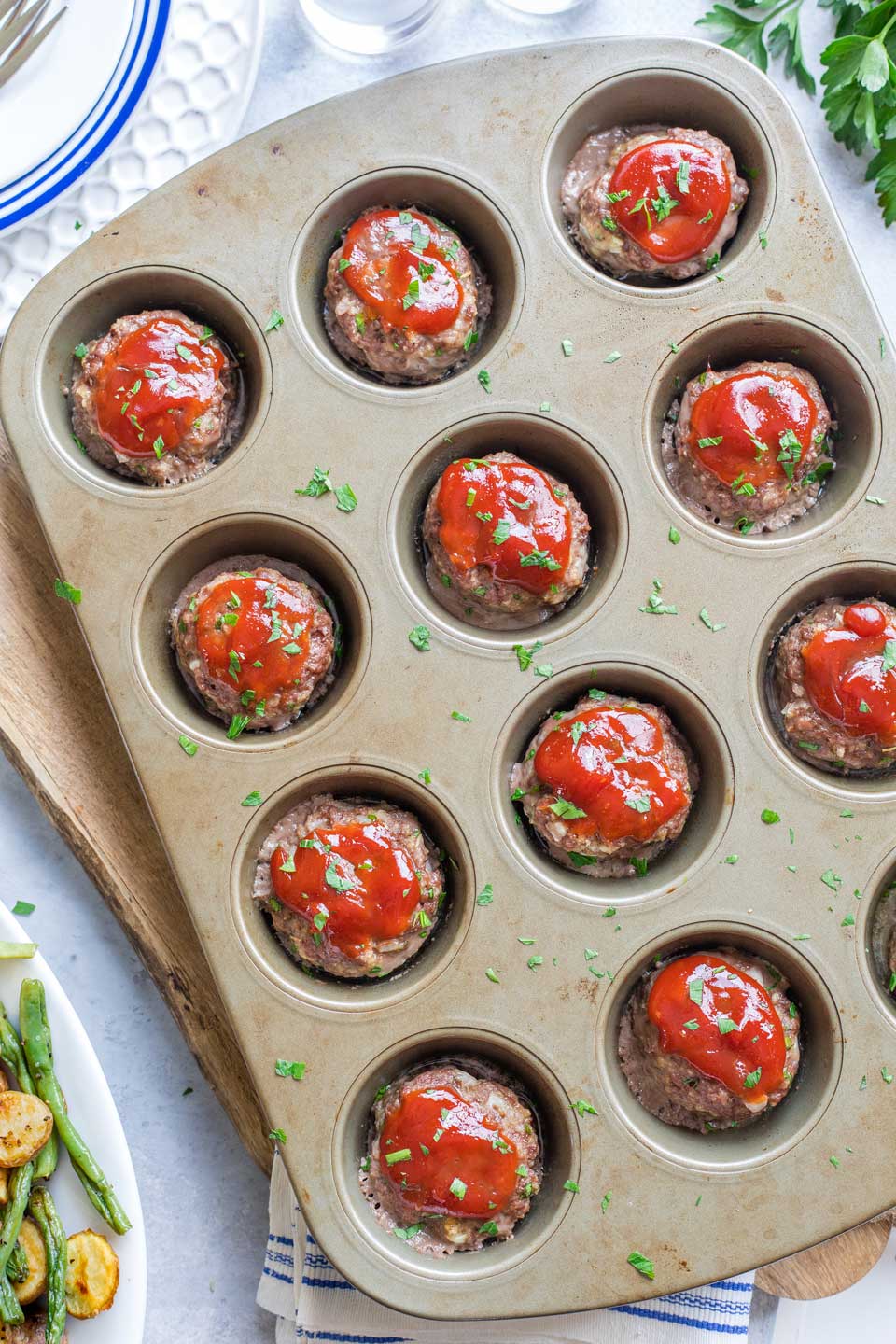 Overhead of full muffin tin after baking, sprinkled with fresh parsley.