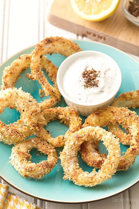 Several onion rings on turquoise plate with little bowl of dipping sauce.