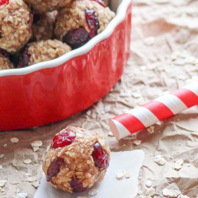 Closeup of one peanut butter energy ball with a striped straw and a red bowl of more balls behind.