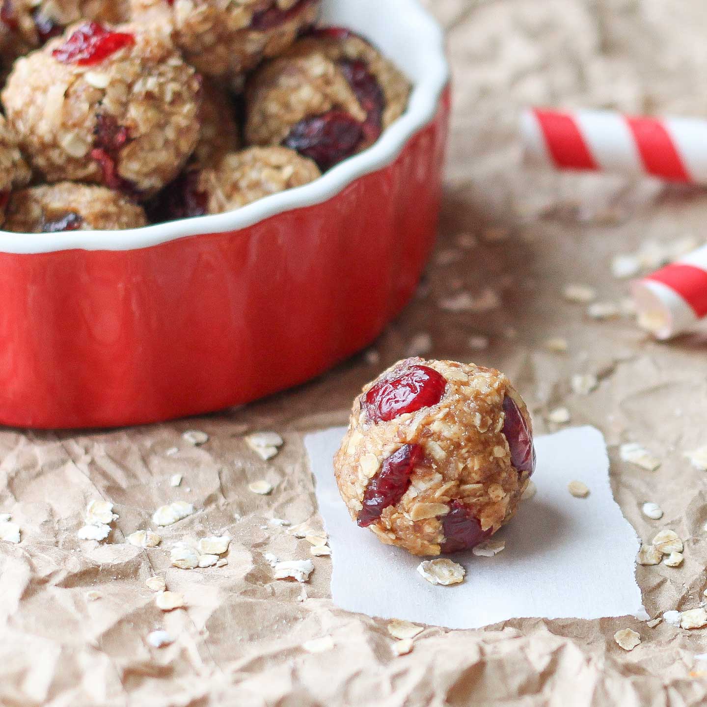 Closeup of one ball on a white paper square on a brown paper backdrop with more energy balls piled in a bowl behind.