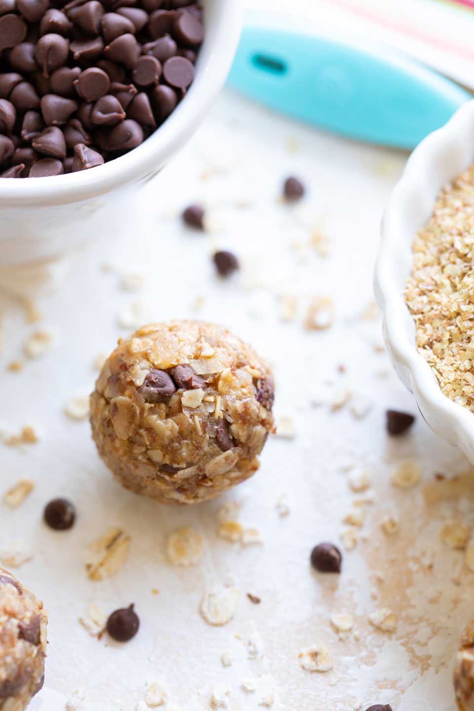 Closeup of one healthy Energy Ball laying between bowls of chocolate chips and wheat germ.