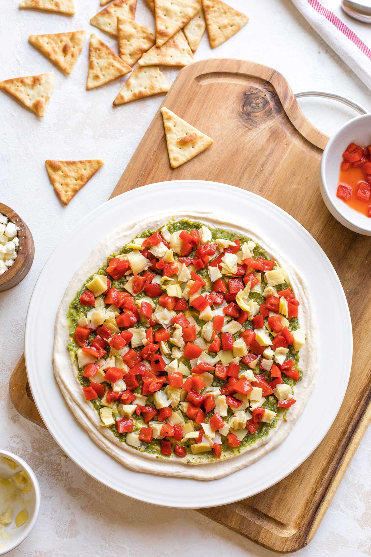 Overhead of artichokes and peppers scattered on top of pesto.