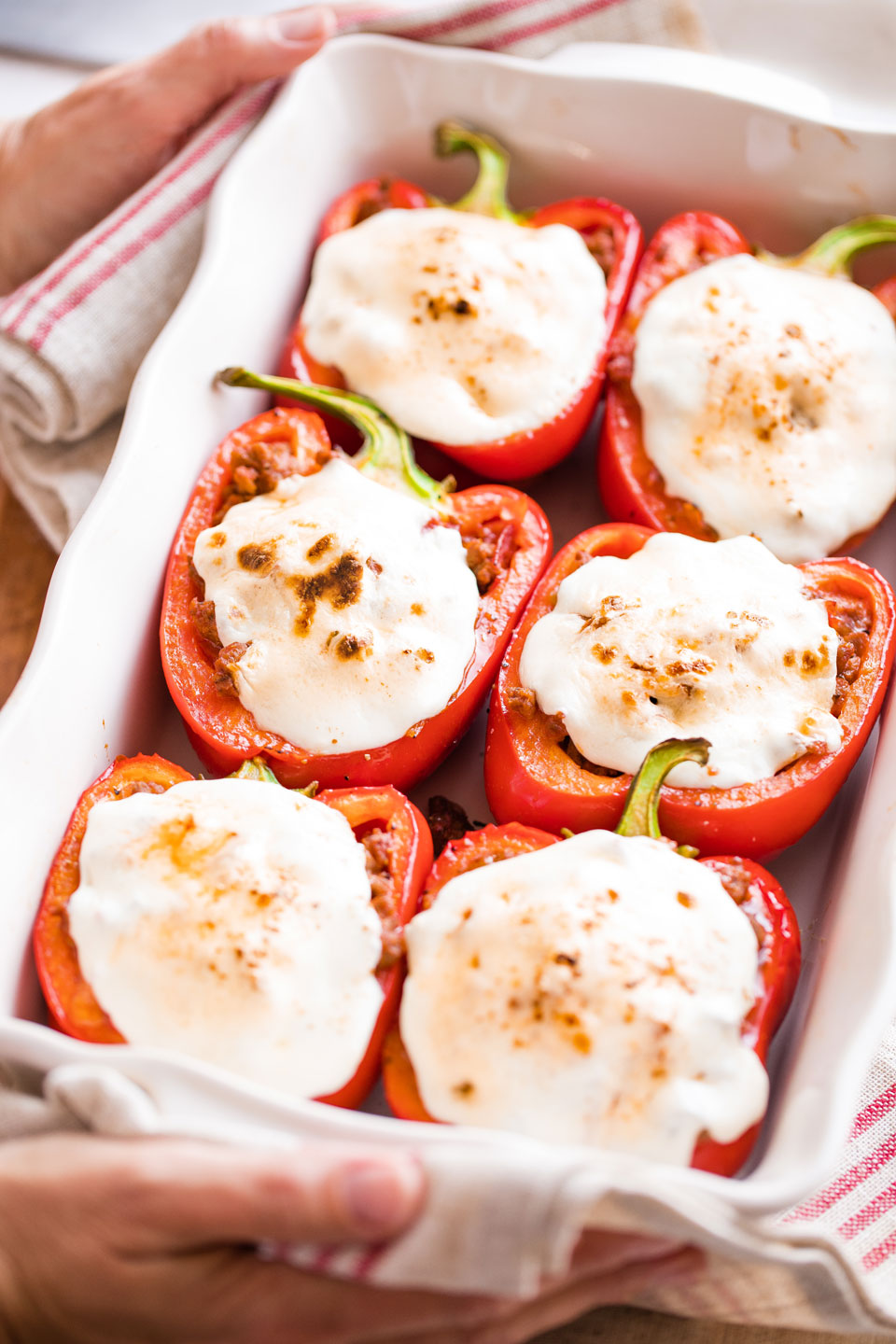 Two hands using striped towels to hold dish of Italian Stuffed Peppers hot from the oven.